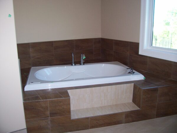 A bathtub with brown tiles around.