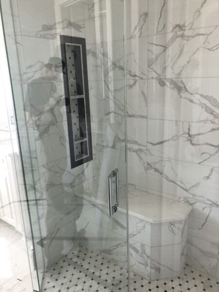 A glass door and white tiles in bathroom.
