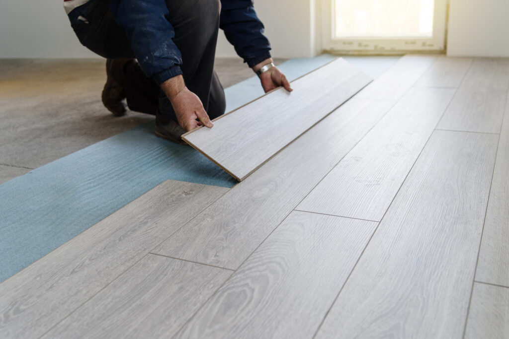 a professiona installing new wood-grain laminate flooring in a home, part of a cost-effective renovation project