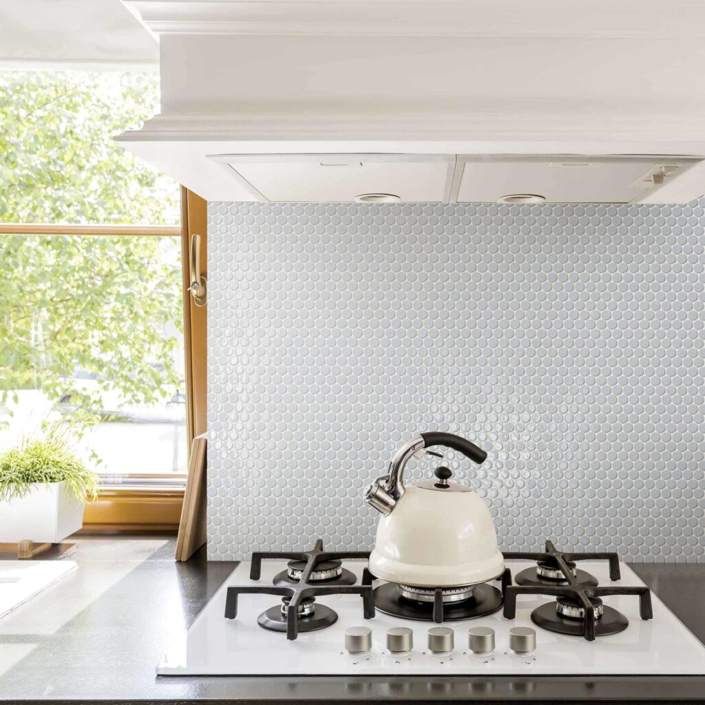 a kitchen backsplash using light grey penny tile, shown behind a white built-in stove top with a white kettle on top