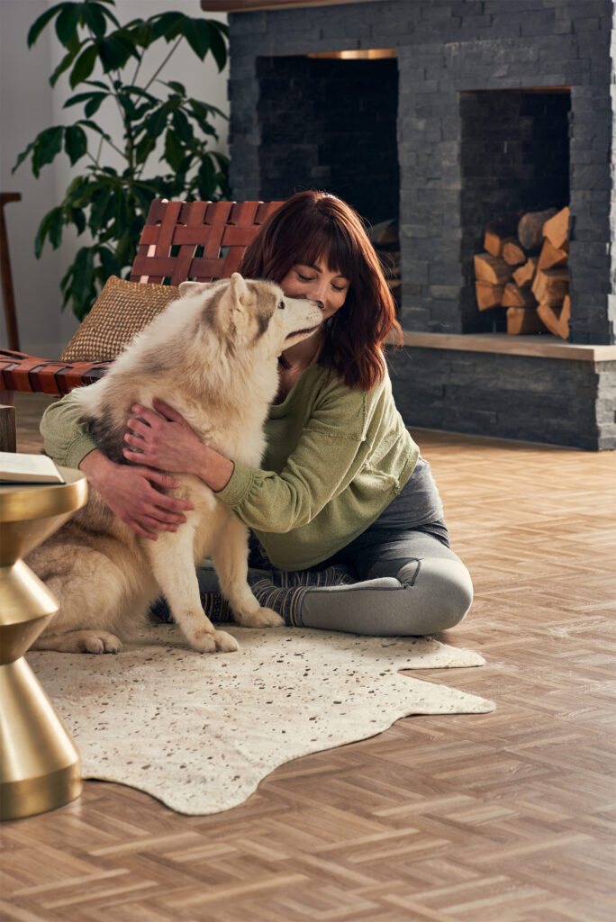 A woman hugging a dog in front of a brick fireplace, in a cozy vacation home with luxury vinyl flooring.