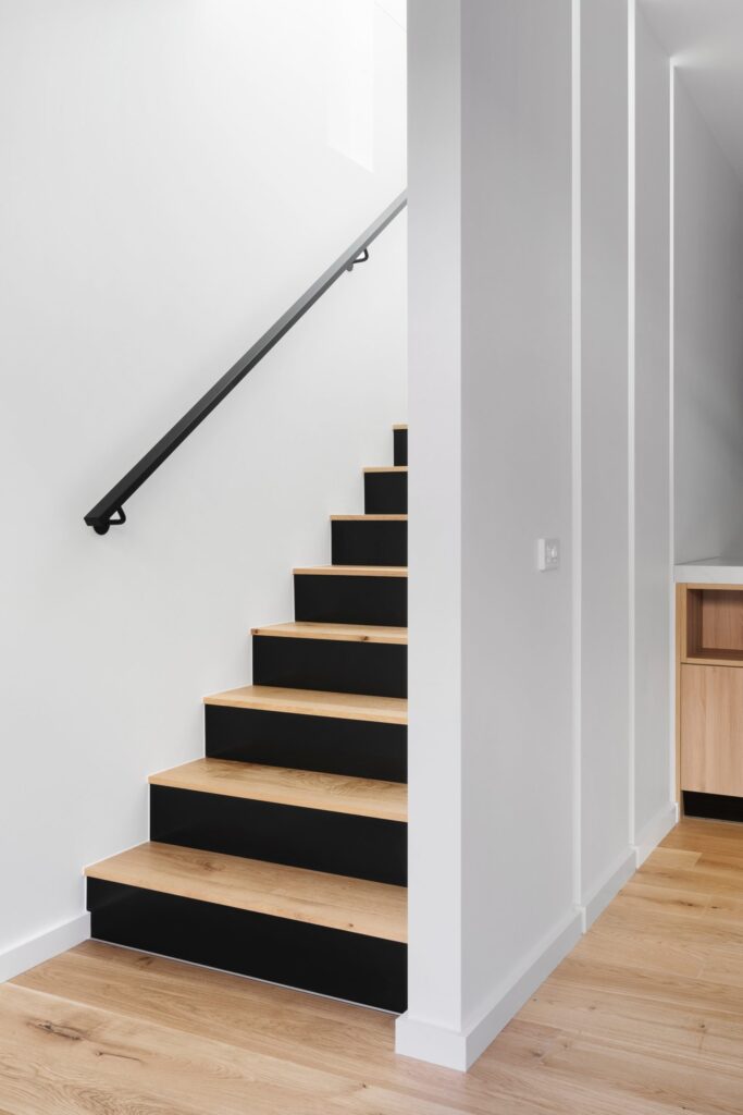 Light woodgrain laminate Flooring on steps with a black base and a black railing against a white wall