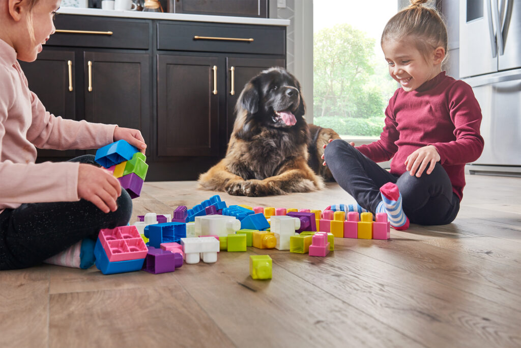 Kids playing with blocks on a floor hardwood floor, with a dog lying in the background; highlighting fall dirt and debris and its impact on wood flooring
