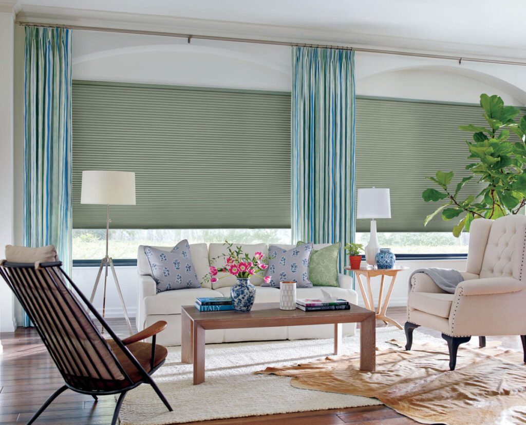 Hunter Douglas green Honeycomb Blinds in a cozy living room, framed by striped blue and green drapes. 