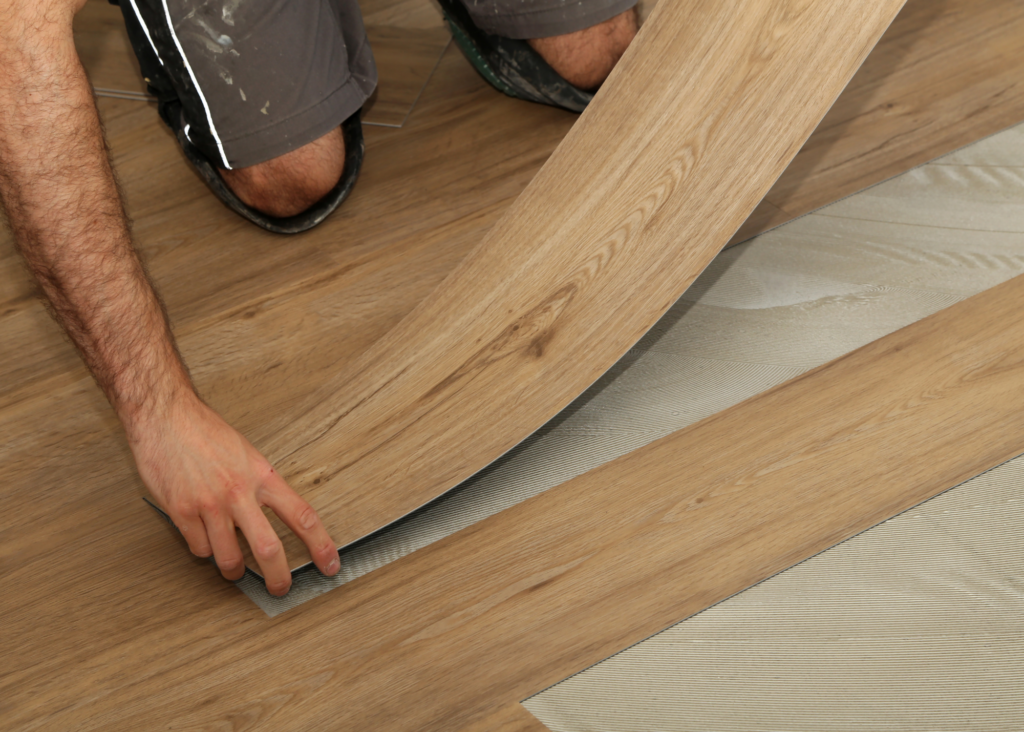 a closeup of a flooring installer putting in luxury vinyl via a glue-down locking system