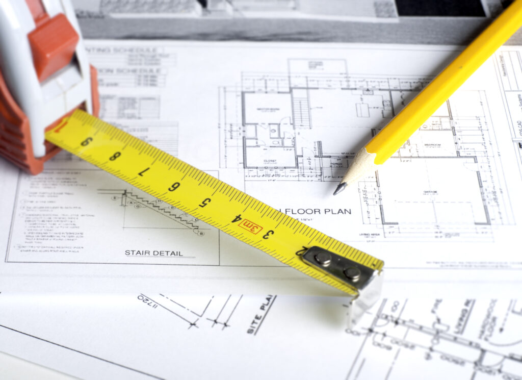 a set of floor plans lying on a desk with a meauring tape and pencil on top, highlighting the illustration tips from our beginner's guide to flooring