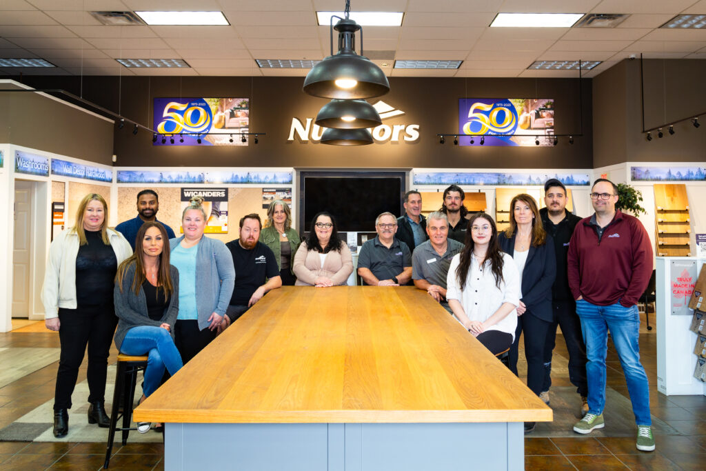 the Nufloors Langley team sitting and standing behind a table in their showroom, with banners highlighting 50 years in business in the background