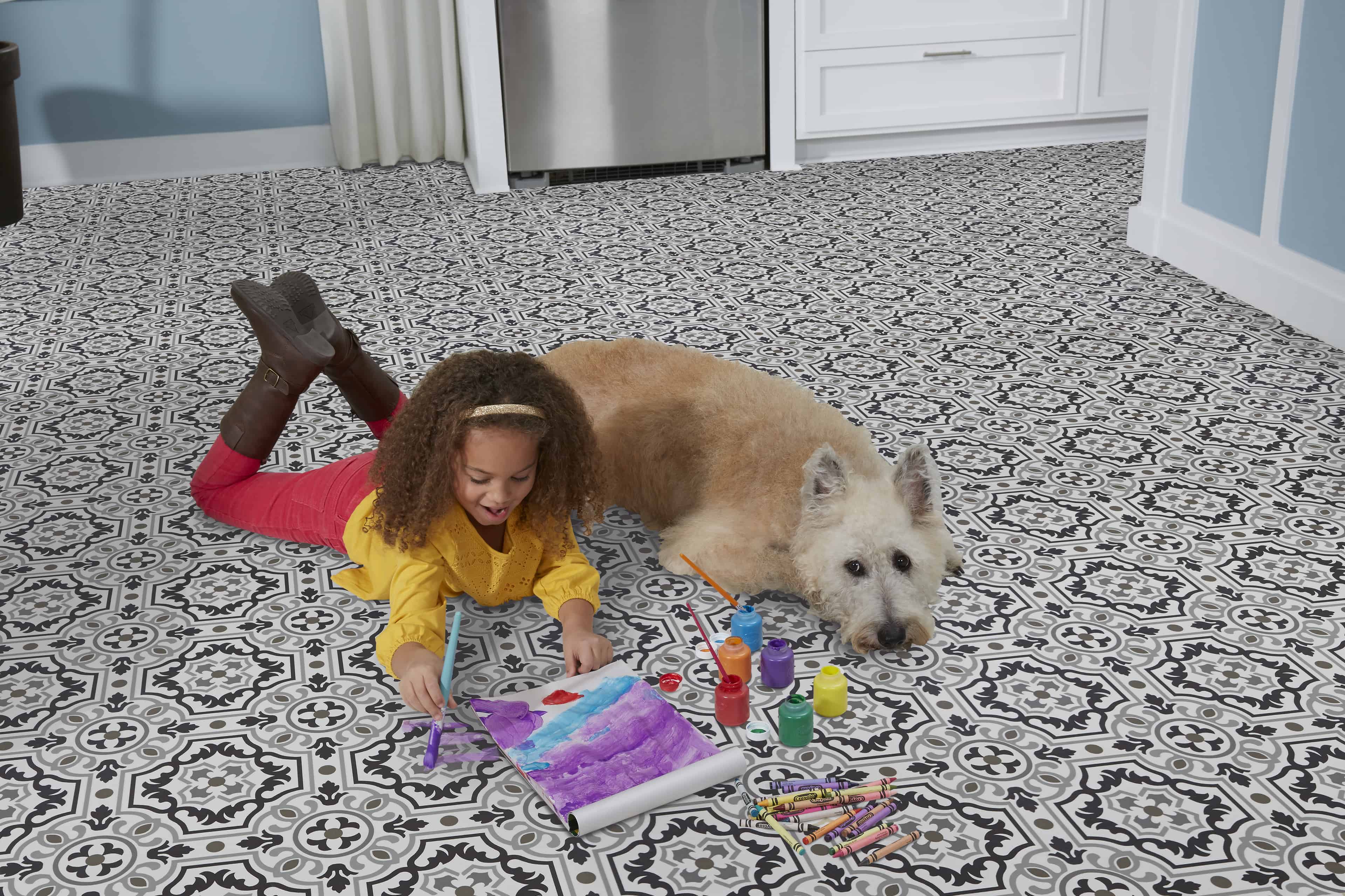 Child laying on floor paining a picture with dog laying beside her; relating to flooring for a busy home.