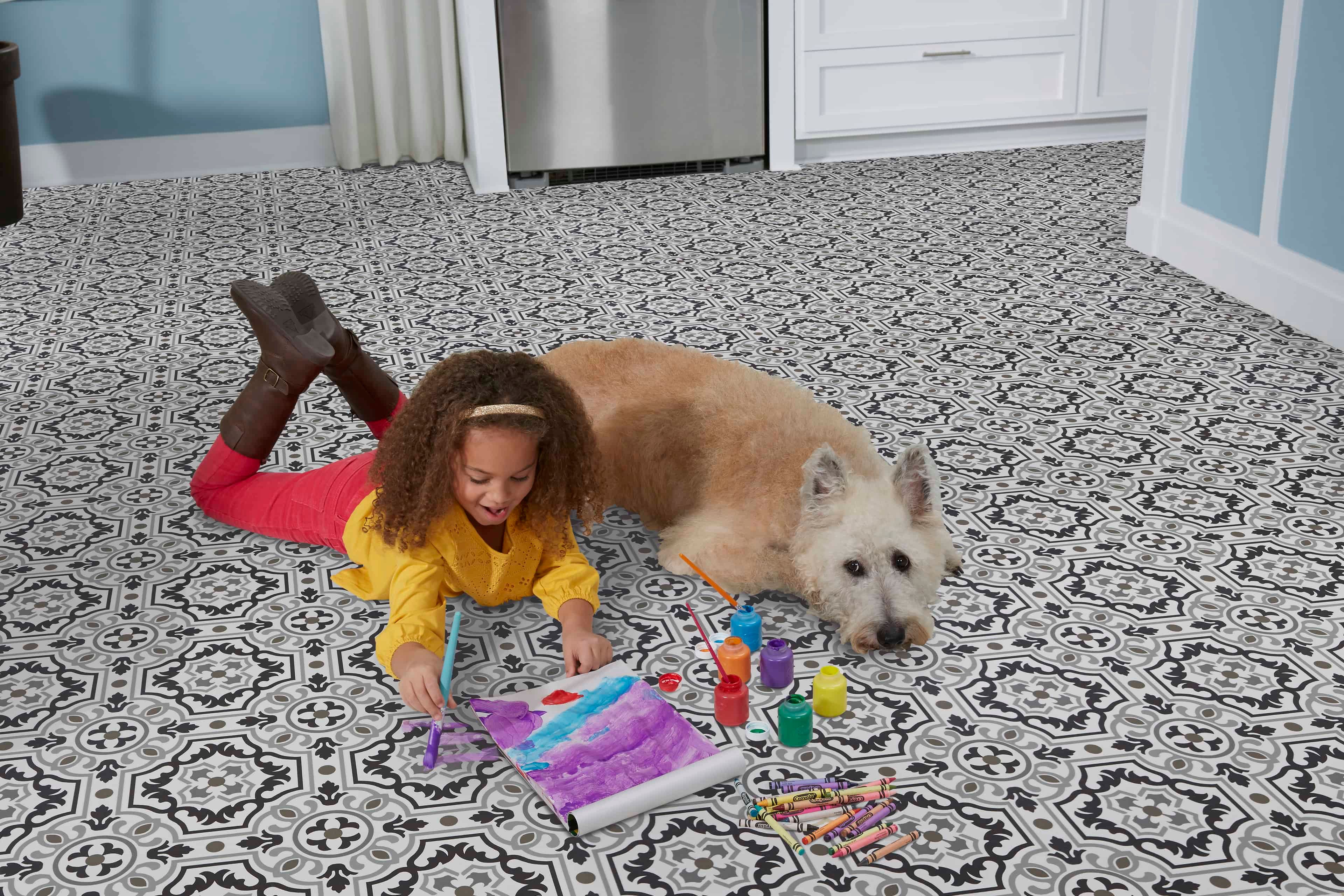 Child laying on floor paining a picture with dog laying beside her; relating to flooring for a busy home.