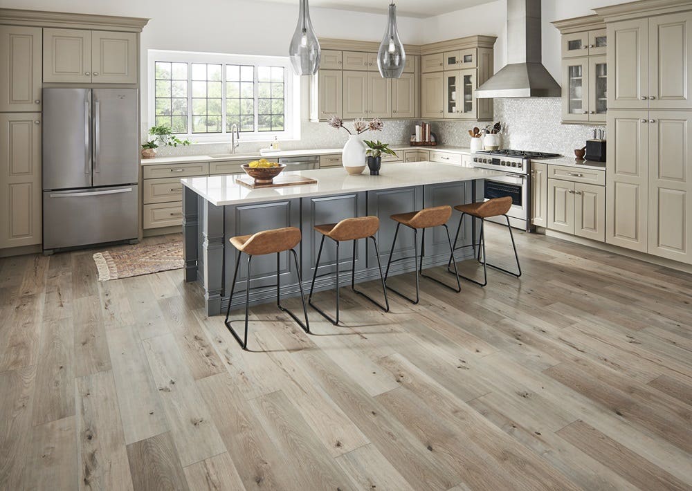 Light floating plank flooring in a modern kitchen with stainless steel appliances, beige cabinets, and pearl white backsplash. 