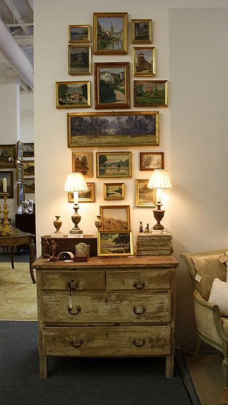 Several small painting on a wall and an antique shelf table.