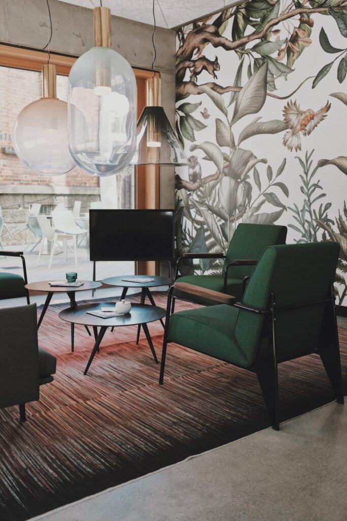 Art Deco style seating in a cafe with large leaf pattern on a feature wall and dark green chairs.