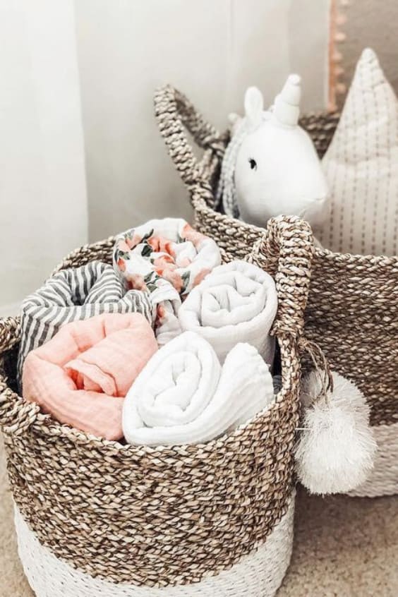Pink, white, grey and floral baby blankets rolled up in baskets in a nursery.