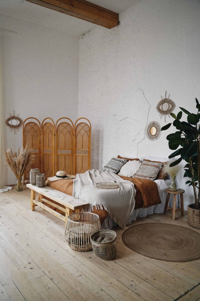 Boho design trends in bedroom with rattan folding screen, sisal rug and pampas grass in a vase.