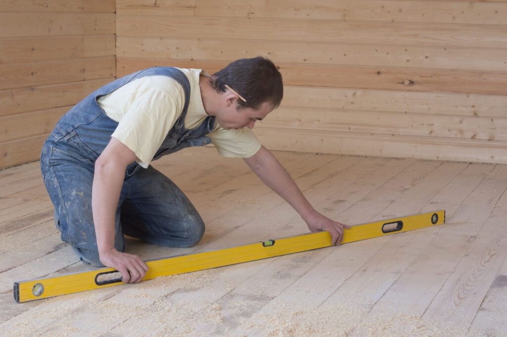a carpenter checking the accuracy of the sub-floor horizon, using a levelling stick in a room of wood plank
