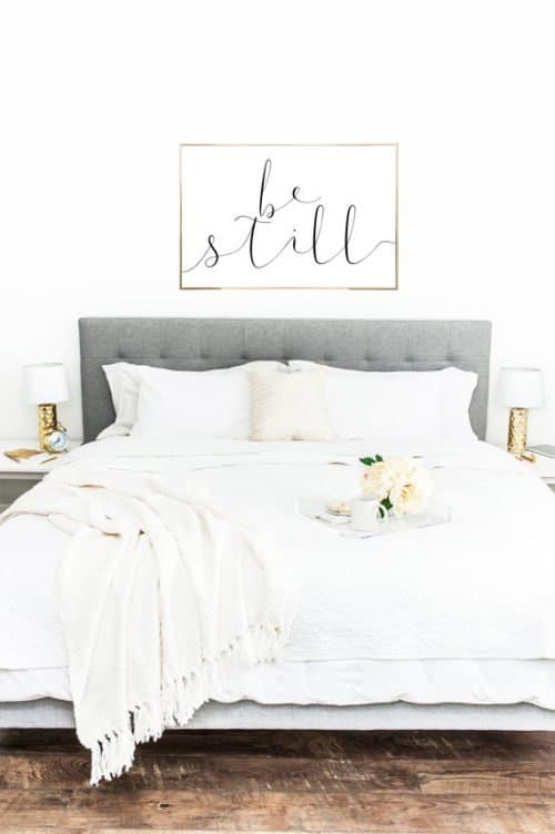 Clean decor look in bedroom with white walls, grey fabric headboard and white bedding.