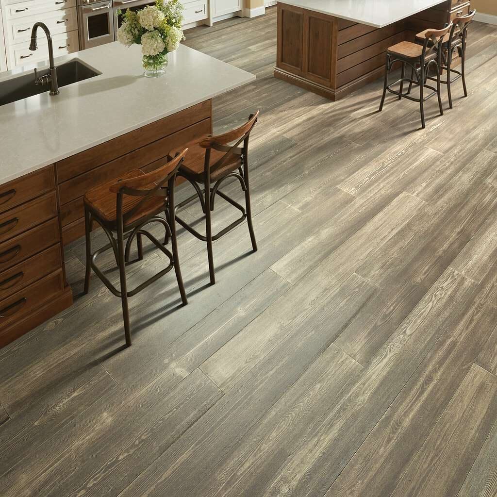 Floating plank flooring in a kitchen with two wooden islands, light grey countertops, and hydrangeas in a vase next to the sink