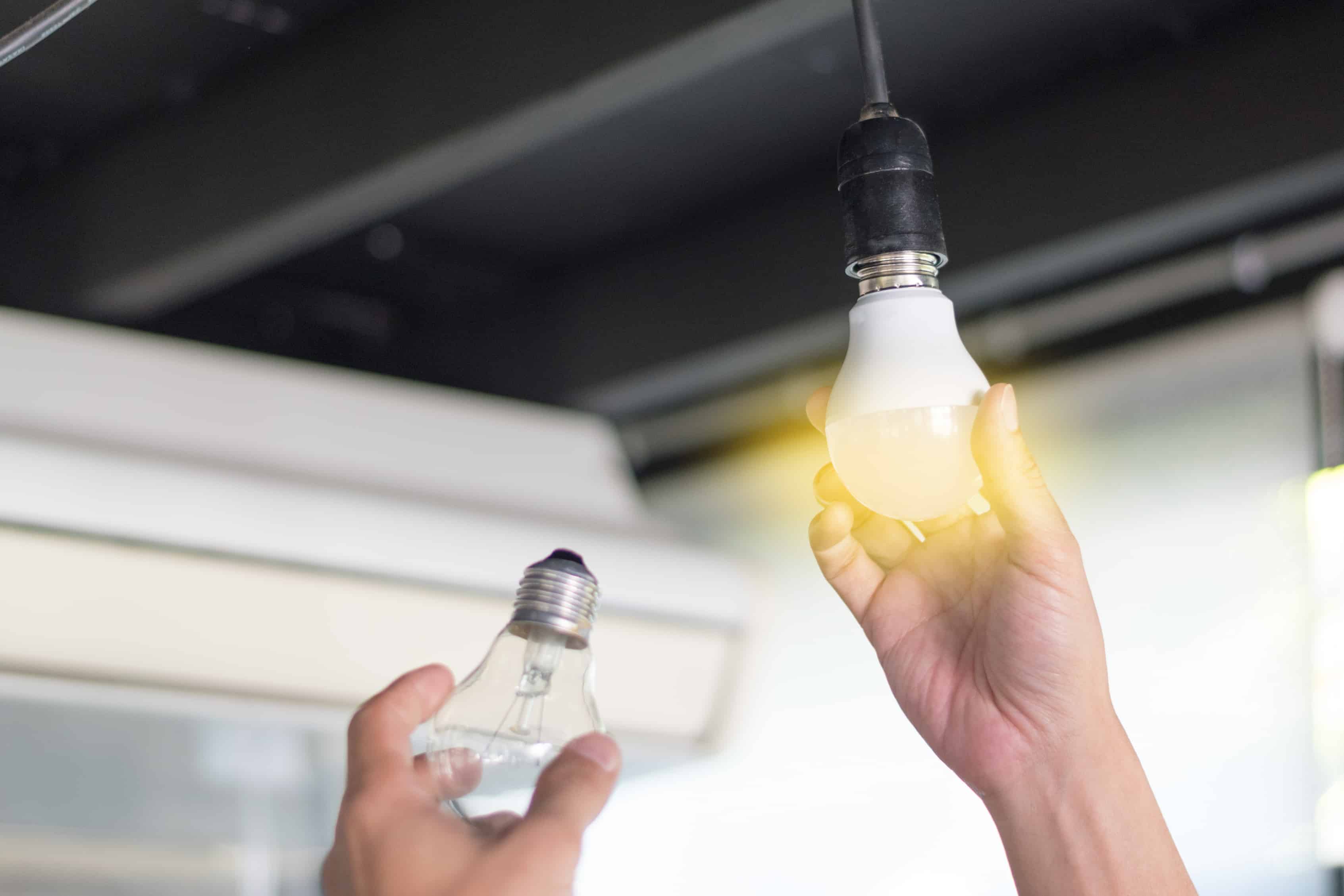 Power saving concept. Man changing compact-fluorescent (CFL) bulbs with new LED light bulb.