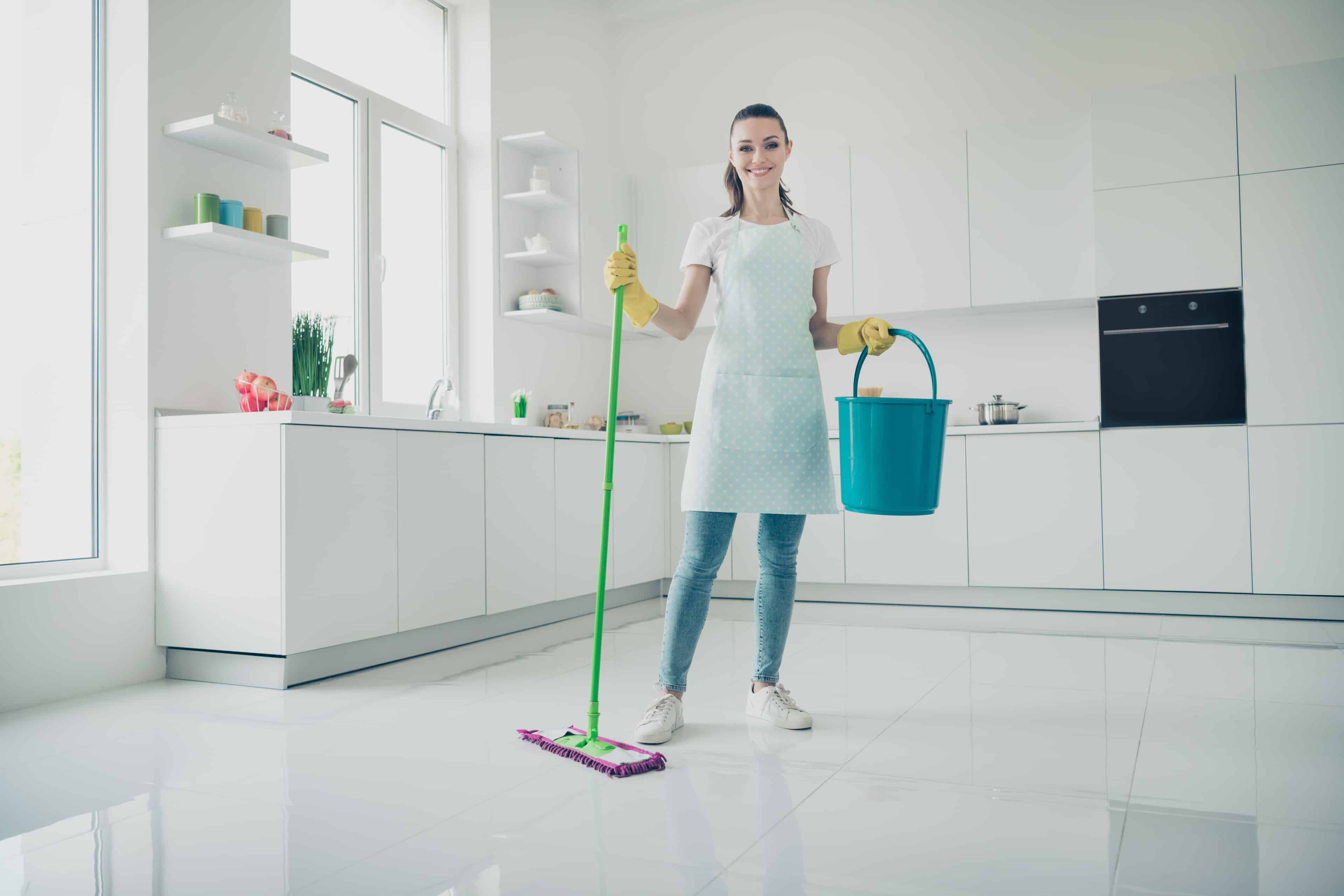 Woman with mop and bucket in kitchen keeping floors clean.