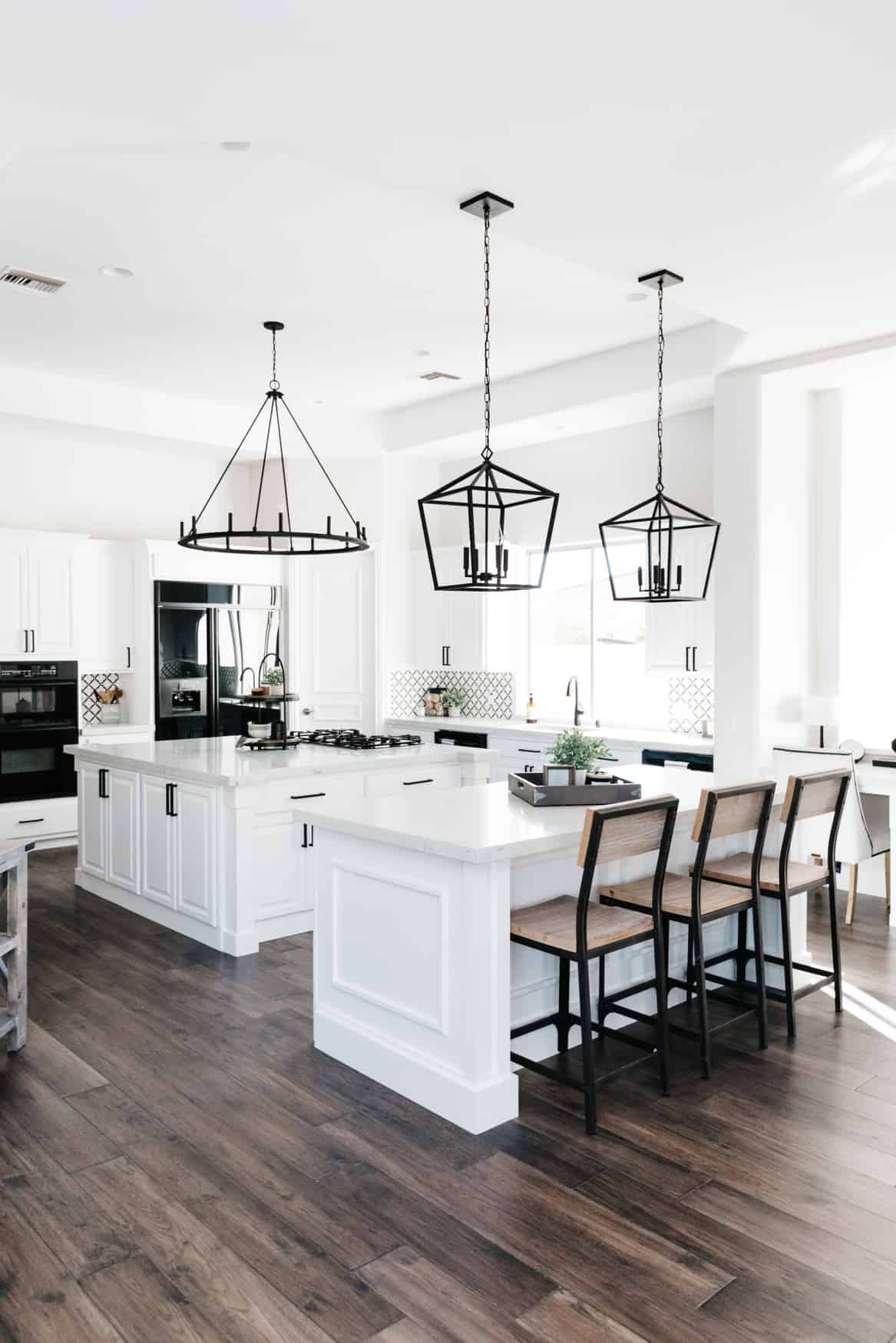 Kitchen with white cabinets, large black pendant lights and dark wood floors.