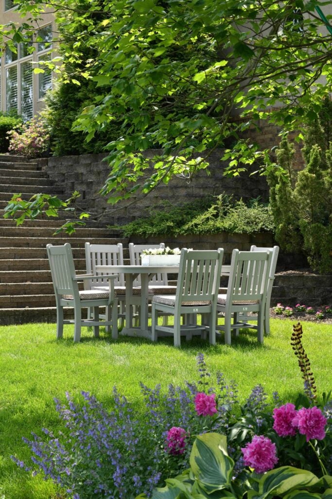 White dining set outdoors in yard on grass with cement steps in the background.