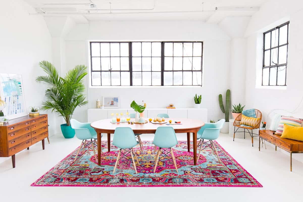 Room with Spring-inspired interior design: white walls, bright pink and blue Persian style rug, and table with modern robin's egg blue chairs.