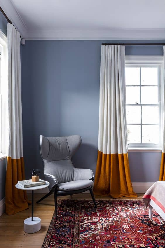 A room with white and orange curtains, a chair, small table and a red carpet; highlighting options for winter decor.