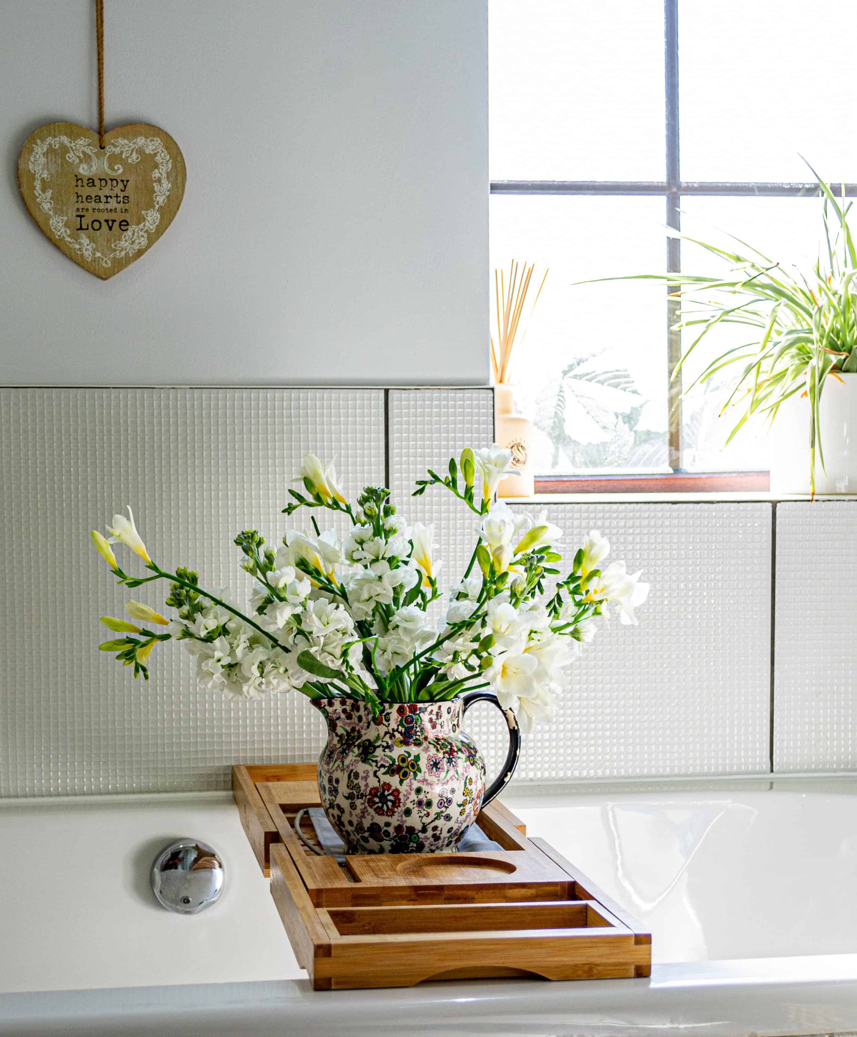 Bathtub with wooden tray across it and spring flowers in a patterned jug.