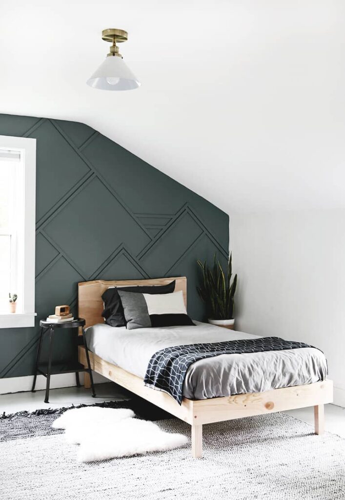 Bedroom with dark green accent wall with wainscoting, light wood bed and black and white area rug.