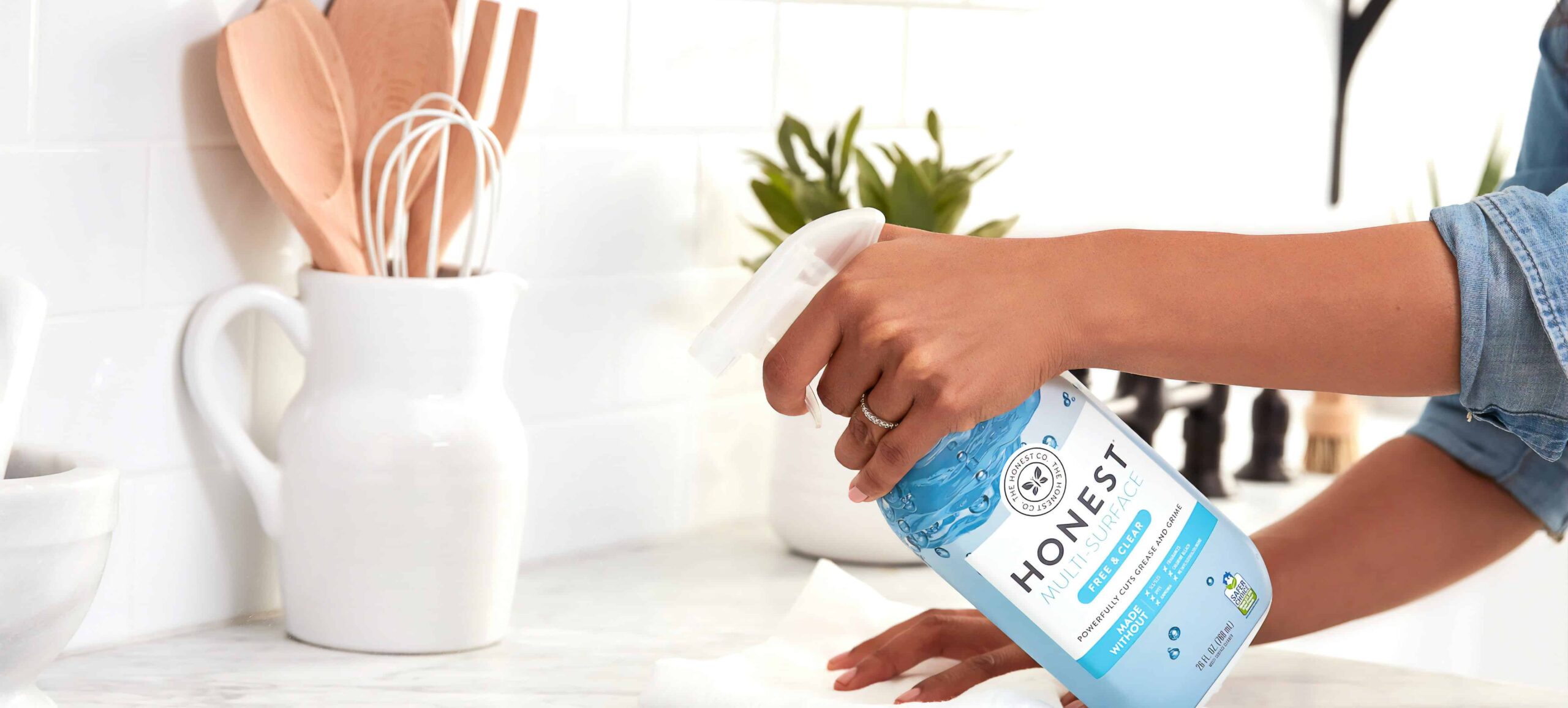 Person spraying Honest Company Multi-surface cleaner on white kitchen counter.