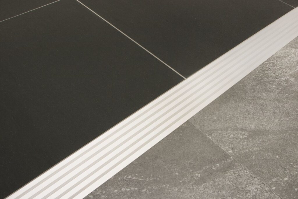 Black ceramic tile and light grey ceramic tile with a white transition strip between them.