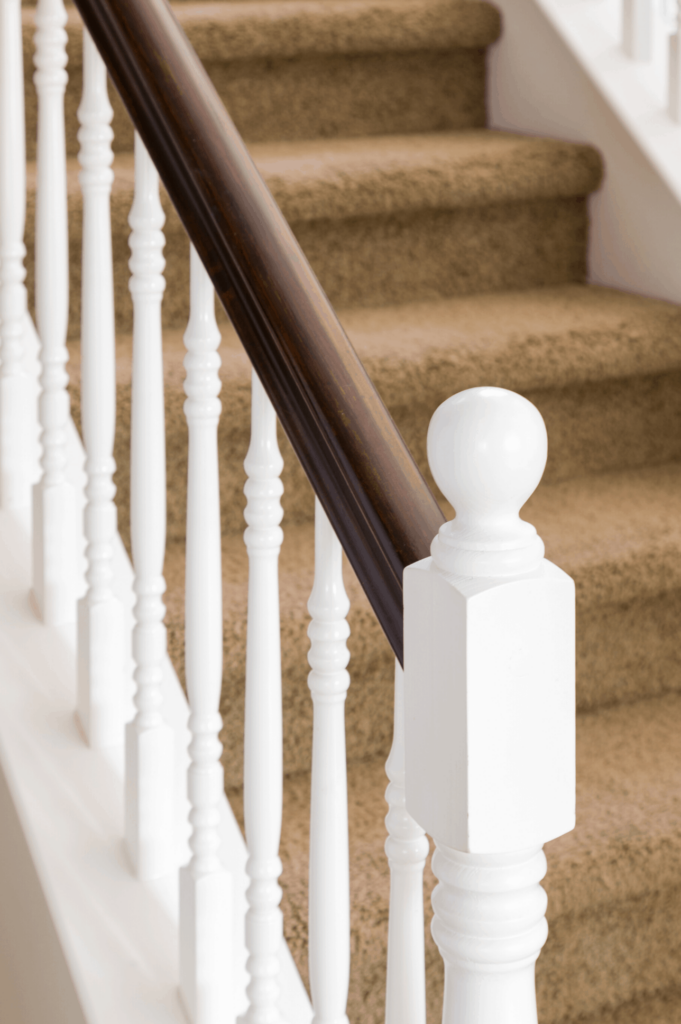 White scrolled wooden stair railing with camel coloured carpet on stairs.